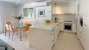 A modern kitchen with a central island, white cabinetry, and stainless steel appliances. - Penthouse 23 - The Cove (Noosa)
