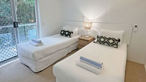 A hotel room with two beds, each with a white duvet and a patterned pillow. There is a bedside table with a lamp between the beds. - Penthouse 23 - The Cove (Noosa)