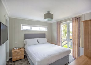 A bedroom with a bed, bedside table, lamp, window, and curtains.