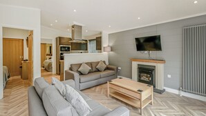 En moderne stue med sofa, sofabord, pejs, fjernsyn og et køkkenområde.