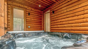 Et interiør af en træhytte med jacuzzi, trævægge og en dør, der fører udendørs.