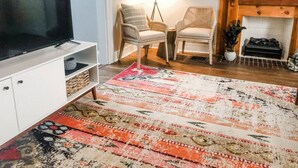 Una sala de estar con una televisión de pantalla plana, dos sillones de mimbre, un tapiz estampado y una chimenea.