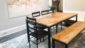 Un comedor con mesa y sillas de madera, un banco y un cuadro abstracto grande en la pared.