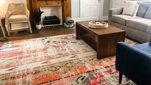 Una sala de estar con chimenea, sofá, mesa de centro y alfombra estampada.