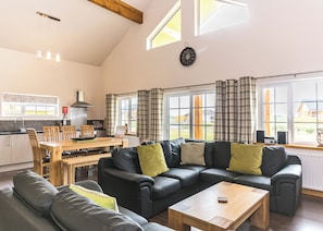 A modern kitchen with a dining area, a black leather sofa, and a wooden coffee table.