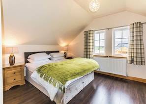A bedroom with a bed, two bedside tables, a lamp, a window with curtains, and a radiator.
