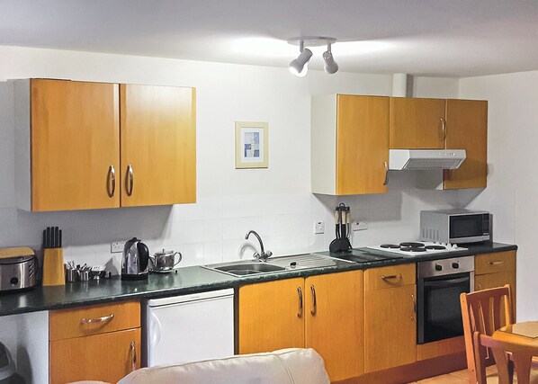A compact kitchen with wooden cabinets, a microwave, a stove, and a sink.