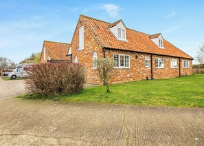 A brick house with a tiled roof, a driveway, and a small tree in the front yard.