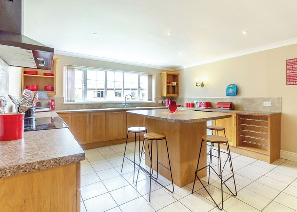 Een keuken met houten kastjes, een groot kookeiland met krukken, een raam en een wandlamp.