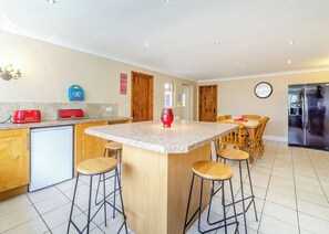 A kitchen with a central island, bar stools, a refrigerator, and a dining area with chairs and a table.
