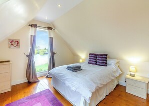 A bedroom with a bed, nightstands, a dresser, a window with curtains, and a view of a body of water.