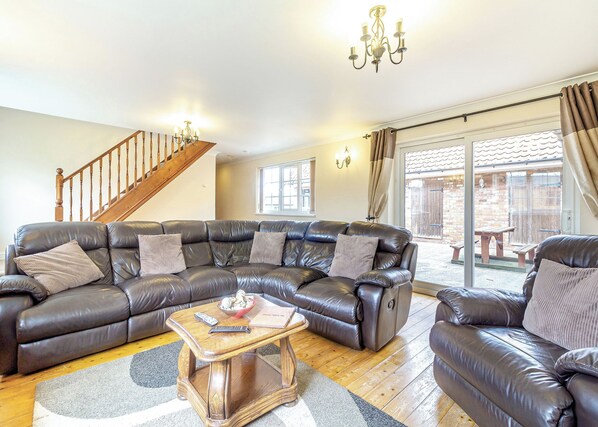 A living room with a leather sectional sofa, a wooden coffee table, a chandelier, and a staircase.
