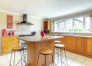 A modern kitchen with a central island, wooden cabinets, a large window, and a red vase. - Three bedroomed holiday cottage. (Swinethorpe, Nr Lincoln)