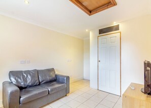 Een kamer met een grijze leren bank, een witte deur, een houten kast en een afstandsbediening op de kast.