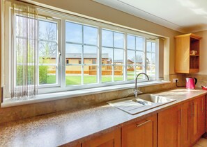 A kitchen with a large window, a sink, and wooden cabinets. - Three bedroomed holiday cottage. (Swinethorpe, Nr Lincoln)