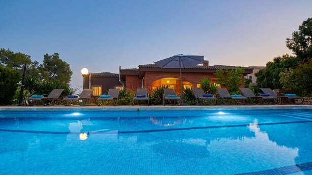 Una piscina con sillones de descanso y un edificio con techo de tejas al fondo.