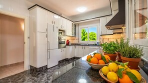 A modern kitchen with white cabinets, a granite countertop, a window with a view of trees, and potted herbs on the counter.