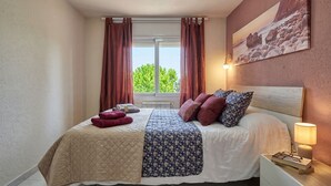 Un dormitorio con una cama, una mesita de noche, una lámpara, una ventana con cortinas y un cuadro en la pared.