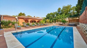 A swimming pool with lounge chairs, a stone wall, and a building with arched windows.