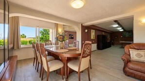 Un comedor con una mesa redonda y sillas, un sofá, y vistas al exterior con vegetación.