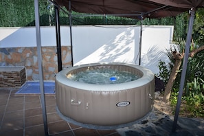 Relax in an outdoor oasis with a hot tub under a shaded canopy, surrounded by lush greenery.