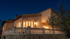 Una casa de fachada de piedra, con un balcón y barandilla, y el interior iluminado.