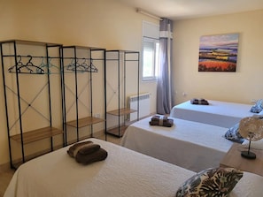Two single beds with bedside tables, a radiator, and a metal wardrobe offer a comfortable and functional space.