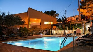 Una piscina con sillones de descanso, un área de estar techada y un edificio con balcón.
