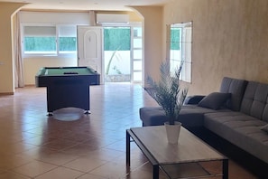Relax in a spacious living area with a pool table, comfortable sofa, and a potted plant.