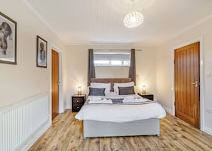 A bedroom with a bed, bedside tables, a hanging light fixture, and a door.