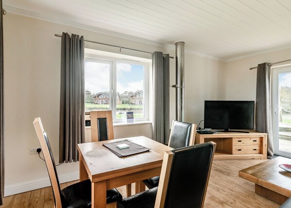 A room with a wooden dining table, chairs, a TV, and a window with curtains.