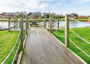 A wooden boardwalk leading to a picnic area with a view of houses and a body of water.