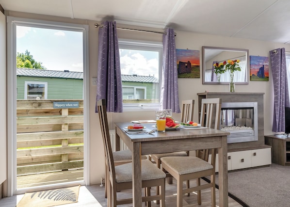 Un coin repas comprenant une table, des chaises, une cheminée et une vue sur une maison, visible à travers une porte vitrée.