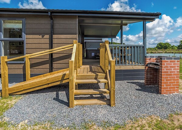 Een houten trap leidt naar een gebouw met een overdekte ingang en een bakstenen gebouw ernaast.