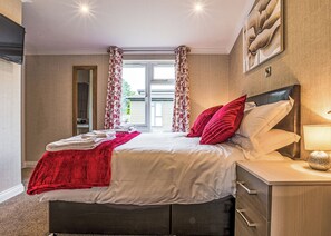 Een slaapkamer met een bed, nachtkastje, lamp en een raam met gordijnen.