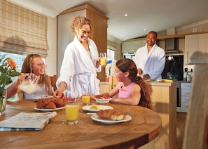 Een familie ontbijt in een moderne keuken met houten kasten, een ontbijttafel met lekkernijen en een aanrecht.