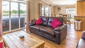 A cozy living room with a leather sofa, wooden coffee table, and a view of the outdoors. - Lakeside 3 Pet Friendly (Woodhall Spa)