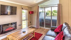 A living room with a fireplace, a sofa, a TV, and a large sliding glass door to the outdoors. - Lakeside 3 Pet Friendly (Woodhall Spa)