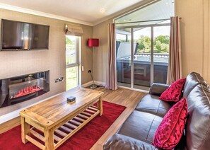 Een woonkamer met een open haard, een bank, een televisie en een grote schuifdeur naar buiten.