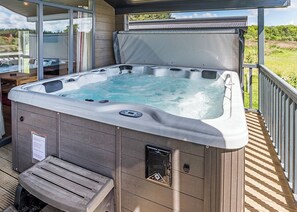 Een hottub op een houten terras, met glazen omheining, bedieningspaneel en een zitbank.