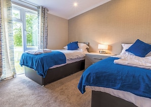 Een hotelkamer met twee bedden, een nachtkastje, een lamp en een raam met gordijnen.