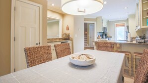 Un comedor con una mesa preparada para dos, una lámpara colgante grande y una cocina al fondo.