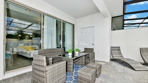 Eine moderne Außenpatio mit Korbmöbeln, einer Glastür, die zu einem Poolbereich führt, und freiem Blick auf den Himmel.