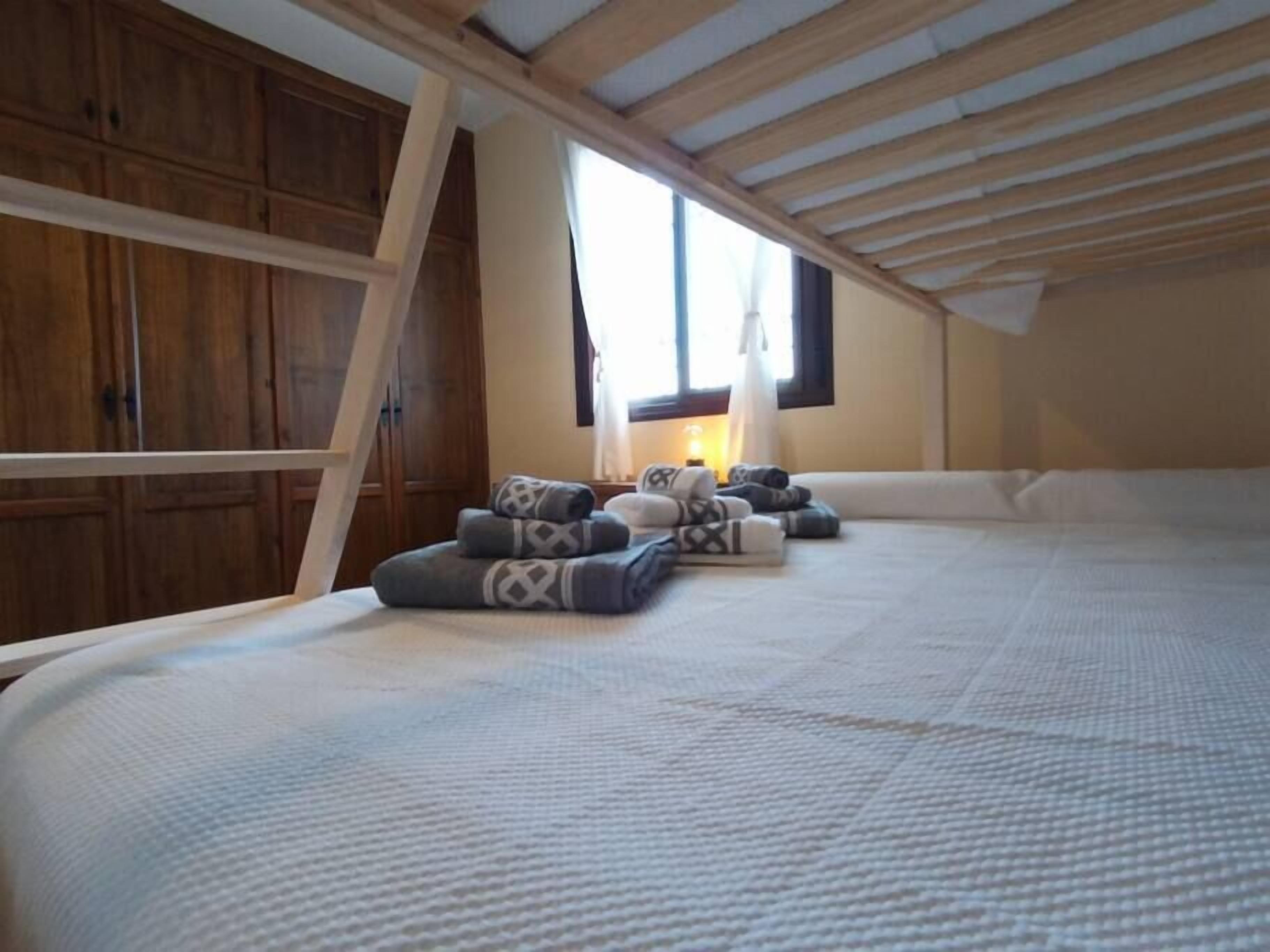 A bedroom with a sloped ceiling, wooden beams, a large window, and a bed with multiple pillows.
