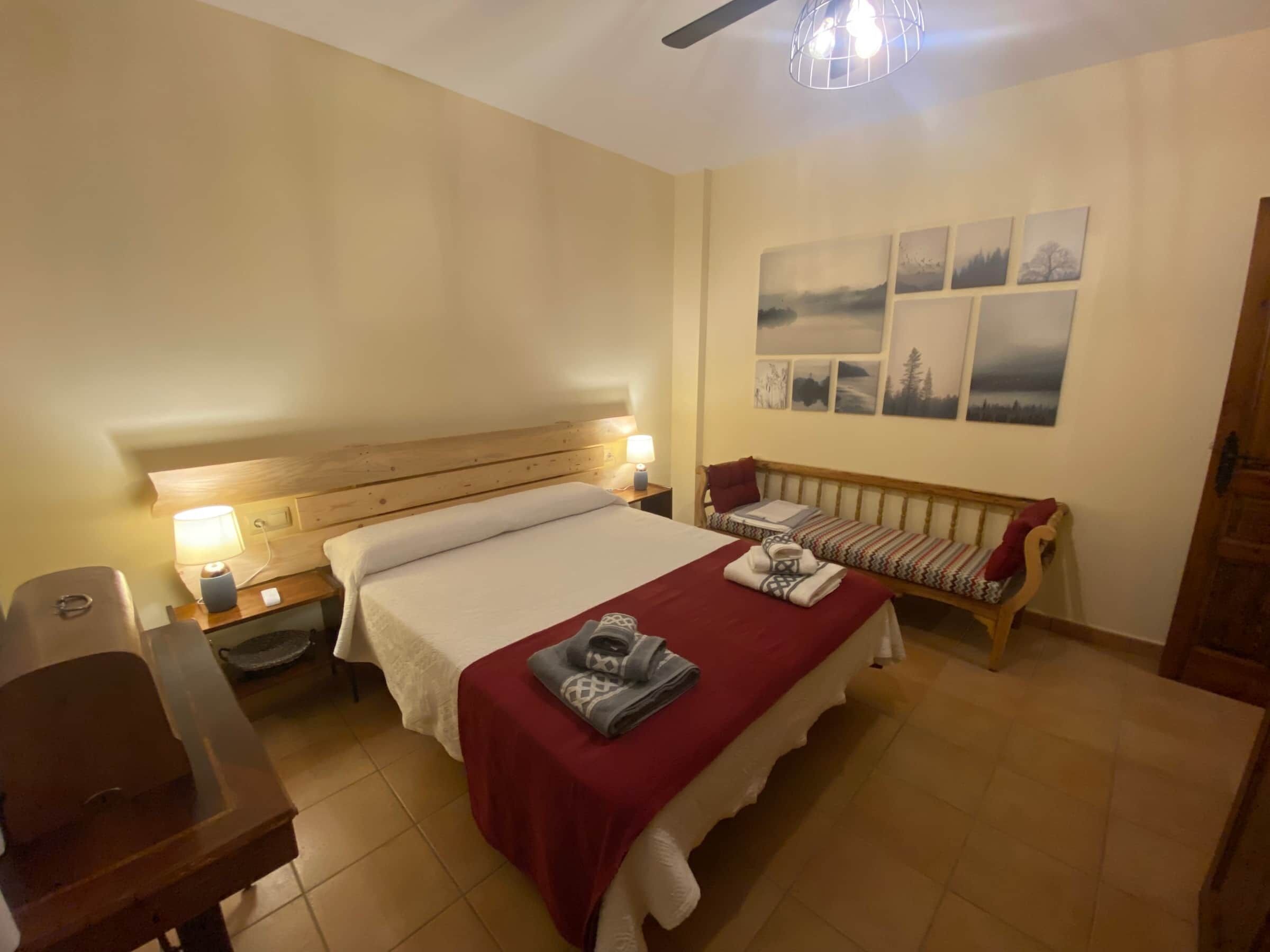 Ein Schlafzimmer mit Bett, Nachttischen, einer Bank und Wandbildern.