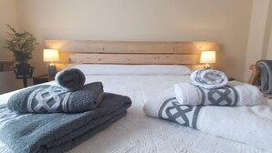 A neatly made bed with a white textured bedspread, two sets of folded towels in grey and white, and a wooden headboard. - Casa Rural El Ojuelo (VTAR) (El Ojuelo)