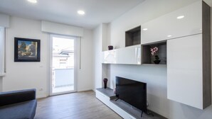 A modern living room with a flat-screen TV, built-in shelves, and a door leading to a balcony. - Vat 52 Sub 16 in Udine (Udine)