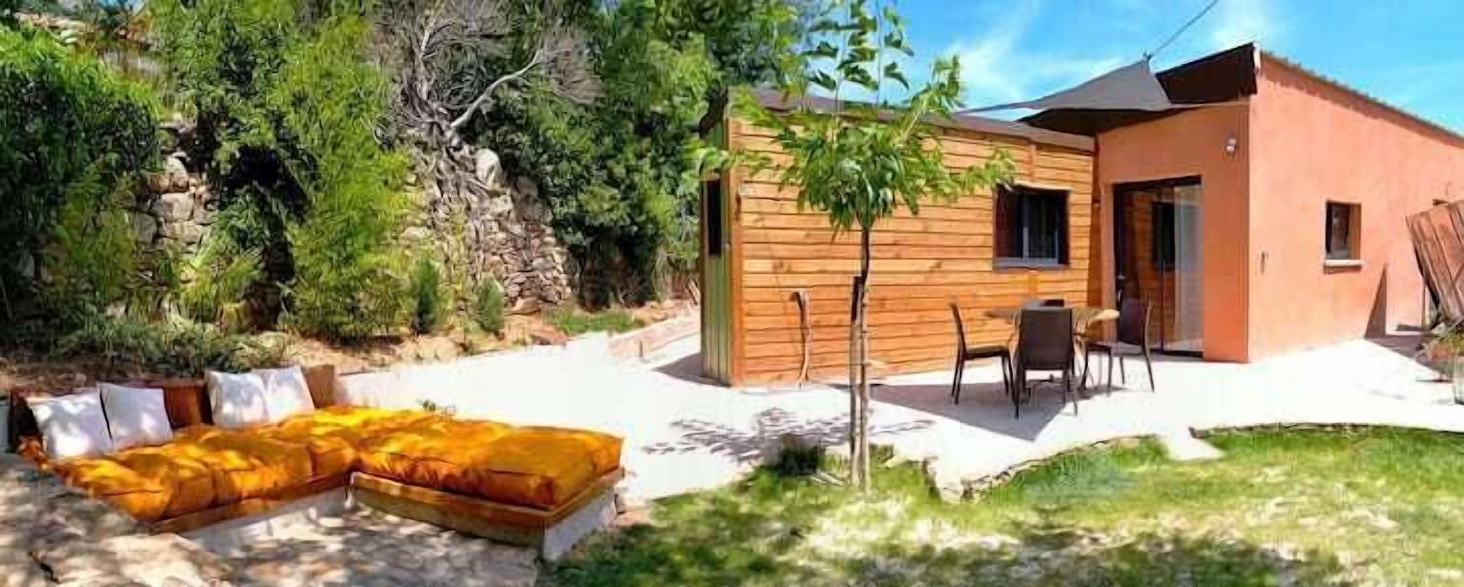 A modern house with a wooden exterior, a patio with outdoor furniture, and a small garden area.