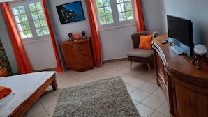 A room with a bed, a chair, a TV, and a cabinet. - La caz à Anne, Villa de Charme (Saint Paul)