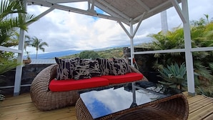 A covered outdoor seating area with wicker furniture and a glass table, overlooking a scenic landscape. - La caz à Anne, Villa de Charme (Saint Paul)